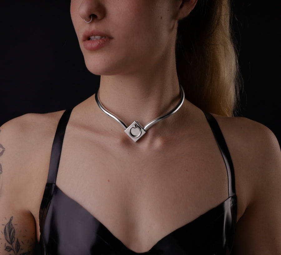 Eine Frau hat einen ergonomischen Halsreif aus Edelstahl an. Dieses Eternity Collar hat einen Ring der O. 