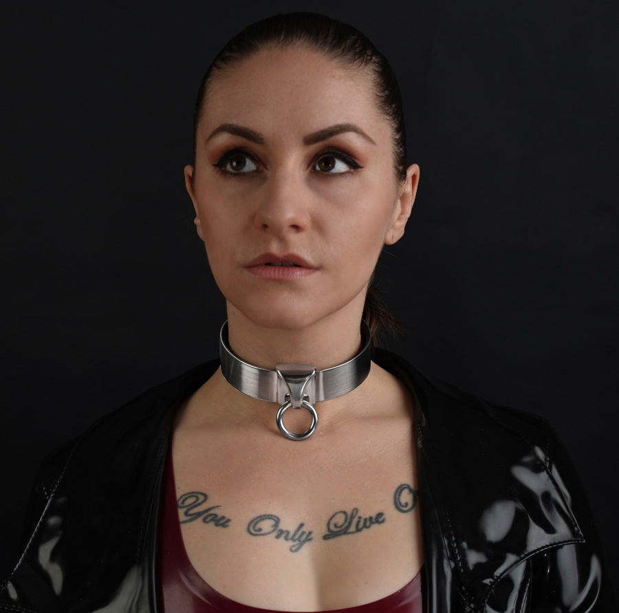 Eine devote Sub hat ein breites devotes BDSM Halsband um den Hals mit Ring der O aus Edelstahl 